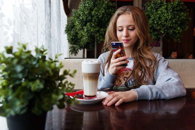 Girl sitting at a table with a coffee looking at Qualcomm's Snapdragon 8 phone